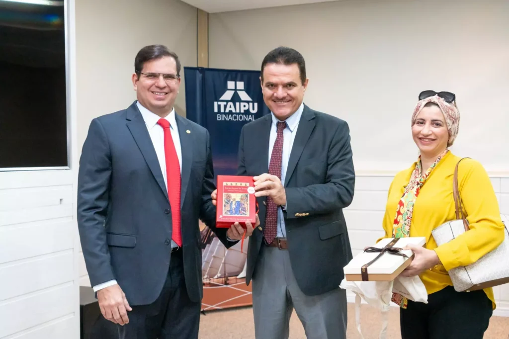 Foto do embaixador junto com o diretor Pepitone segurando o presente vermelho. Legenda: Troca de presentes entre o diretor Pepitone e o embaixador.