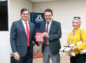 Foto do embaixador junto com o diretor Pepitone segurando o presente vermelho. Legenda: Troca de presentes entre o diretor Pepitone e o embaixador.
